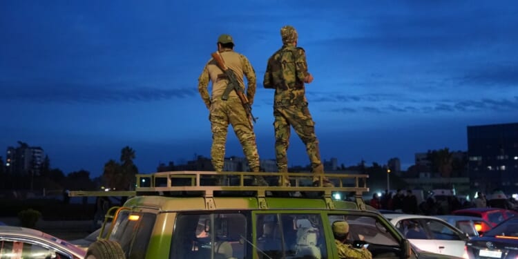 Syrian soldiers stand on a car.