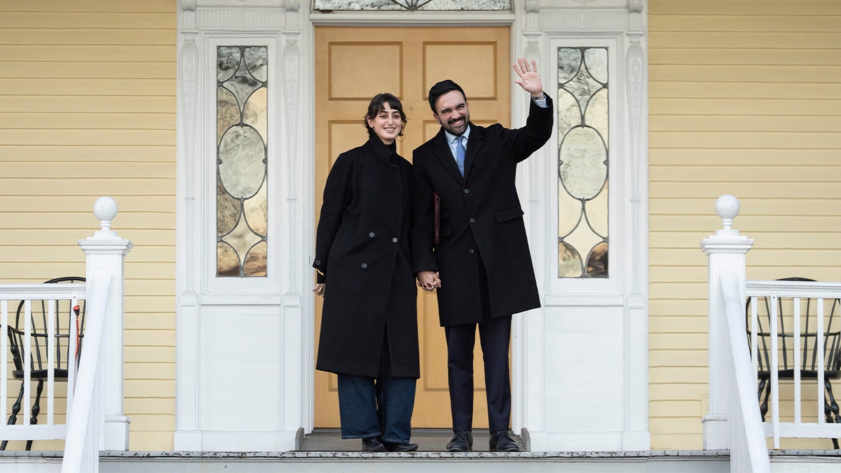 NYC Mayor Zohran Mamdani waves and holds his wife's hand in front of Gracie Mansion