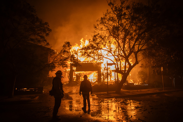 Firefighters watch the flames from the Palisades Fire burning a home during a powerful windstorm