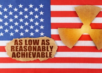 Industry and radiation concept. On the flag of the United States, there is a symbol of radioactivity and a torn cardboard with the inscription - As Low As Reasonably Achievable ALARA