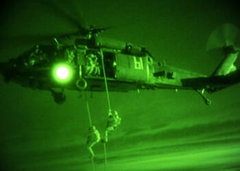 Two Delta Force soldiers descending from a helicopter.