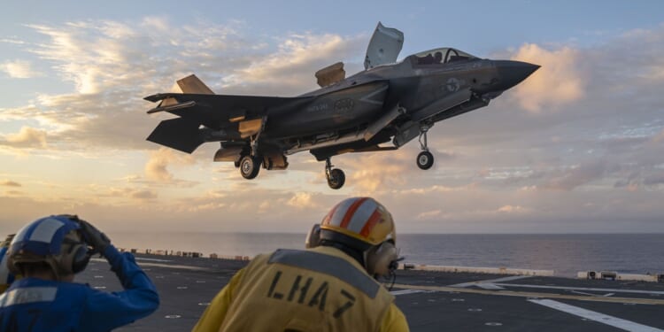 An F-35B fighter jet lands on the deck of an aircraft carrier.