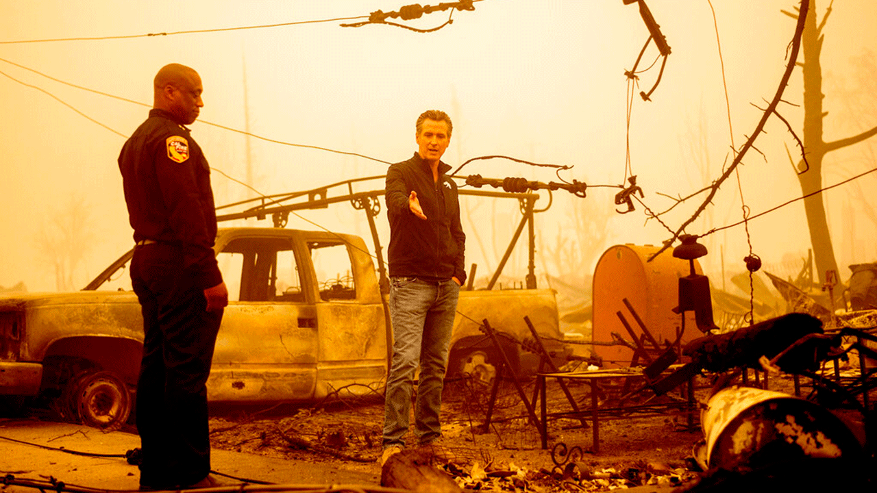 California Gov. Gavin Newsom examines a scorched utility pole while surveying fire damage.