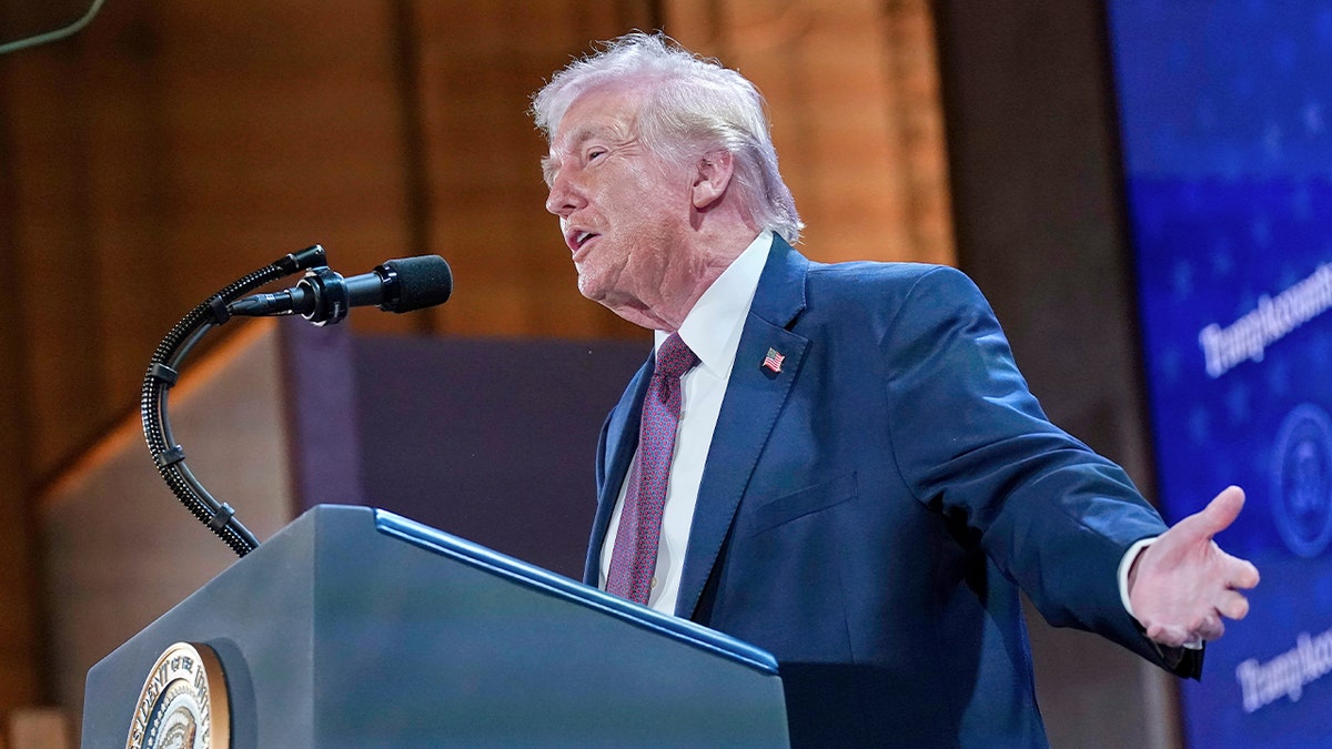 Trump speaks into a microphone with his arms out to the side and back, as he is gesturing