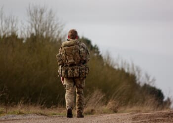 A British soldier walking on a dirt road.