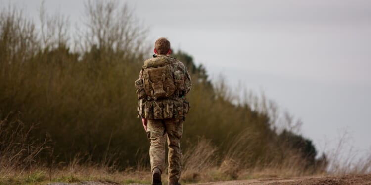A British soldier walking on a dirt road.