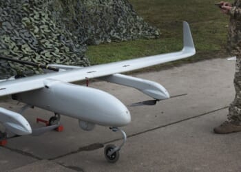 A military drone next to a man in uniform.
