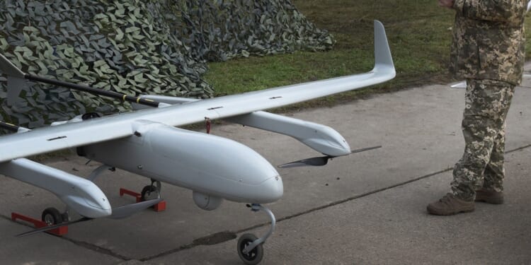 A military drone next to a man in uniform.