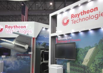 Raytheon's booth at an arms show, showing missiles and fighter aircraft.