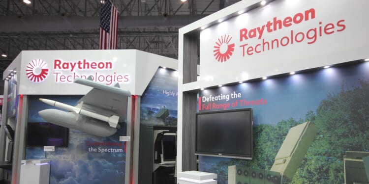 Raytheon's booth at an arms show, showing missiles and fighter aircraft.