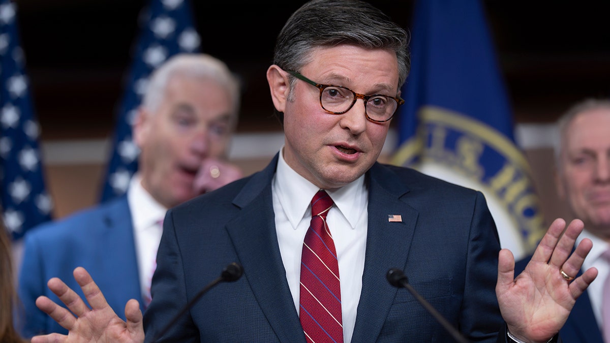 Speaker Mike Johnson gesturing with his hands while speaking to a group of reporters.