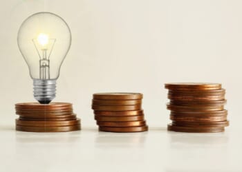 Increasing of electricity cost for residential and business users, expensive energy bill and rise in electricity prices concept. Lots of coins and a light bulb