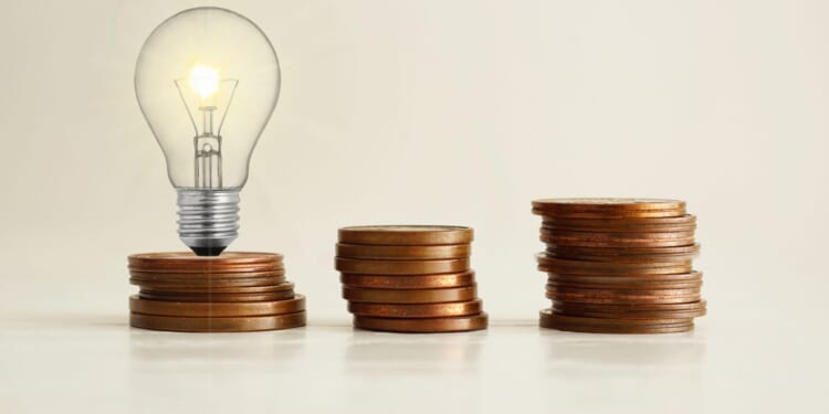 Increasing of electricity cost for residential and business users, expensive energy bill and rise in electricity prices concept. Lots of coins and a light bulb