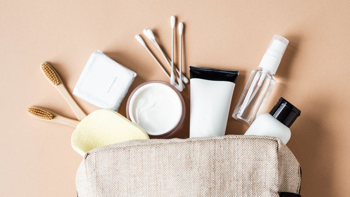 Travel cosmetic bag with the necessary means to care for women's skin. Cosmetics, dry shampoo, cotton buds, toothbrushes next cosmetic bag on a beige background. top view