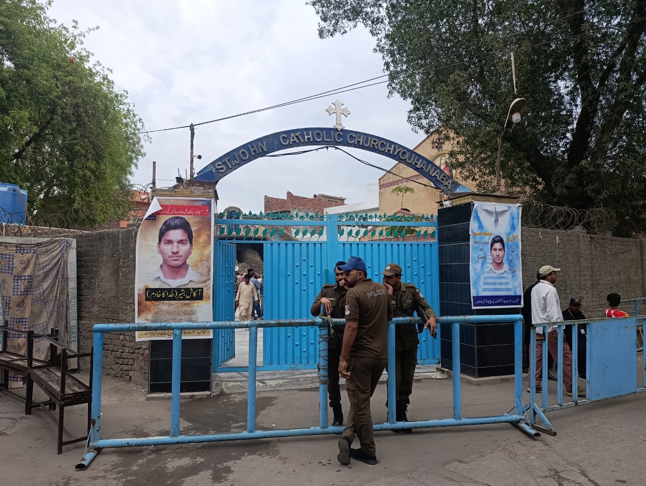 Pakistani police stand guard outside St. John’s Catholic Church in Youhanabad, Lahore, on March 15, 2025. Posters of Servant of God Akash Bashir flank the entrance gate on the 10th anniversary of twin suicide bombings that struck the neighborhood. | Credit: Kamran Chaudhry