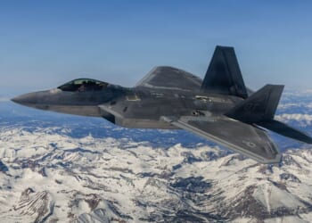 An F-22 Raptor in flight over a snowy mountain.