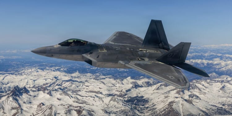 An F-22 Raptor in flight over a snowy mountain.
