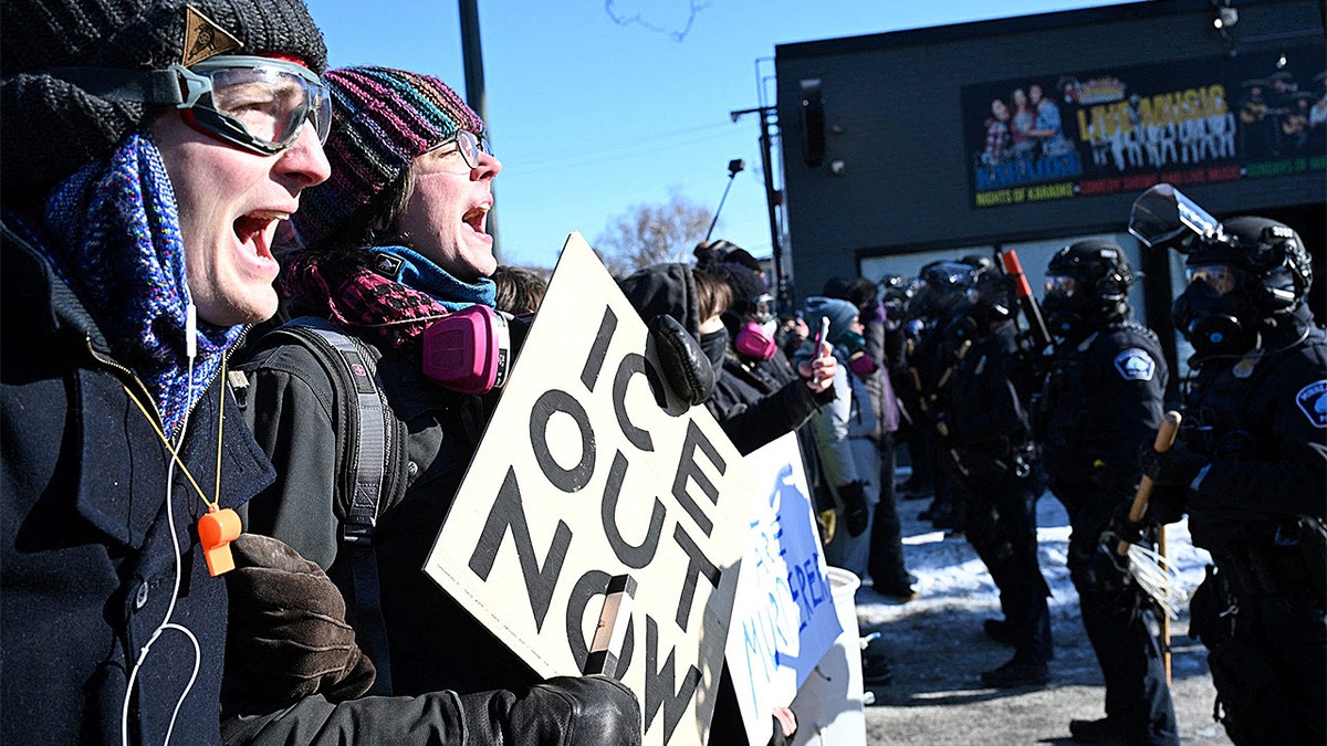 Protesters holding whistles and facing off with Minneapolis police officers on a street.