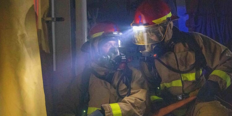 Two Navy firefighters using a hose.