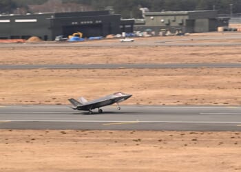 An F-35 landing on a runway next to two dry fields.