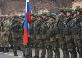 Russian soldiers standing at attention near a Russian flag.