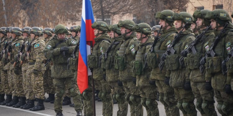 Russian soldiers standing at attention near a Russian flag.