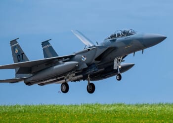 An F-15EX fighter jet taking off near a grassy hill.