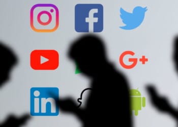 Silhouetted users are shown looking at their phones against a backdrop of major social media platform logos.