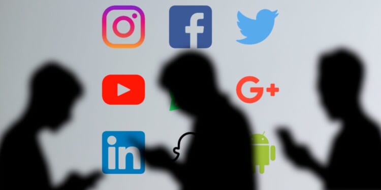 Silhouetted users are shown looking at their phones against a backdrop of major social media platform logos.