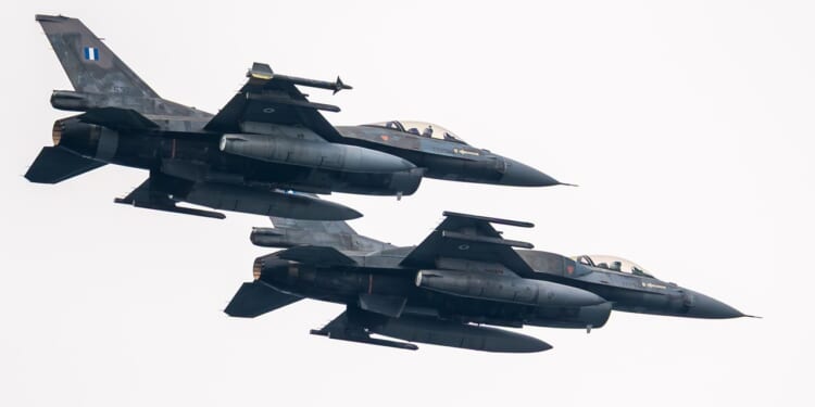 Two F-16s with Greek markings flying next to each other against a white sky.