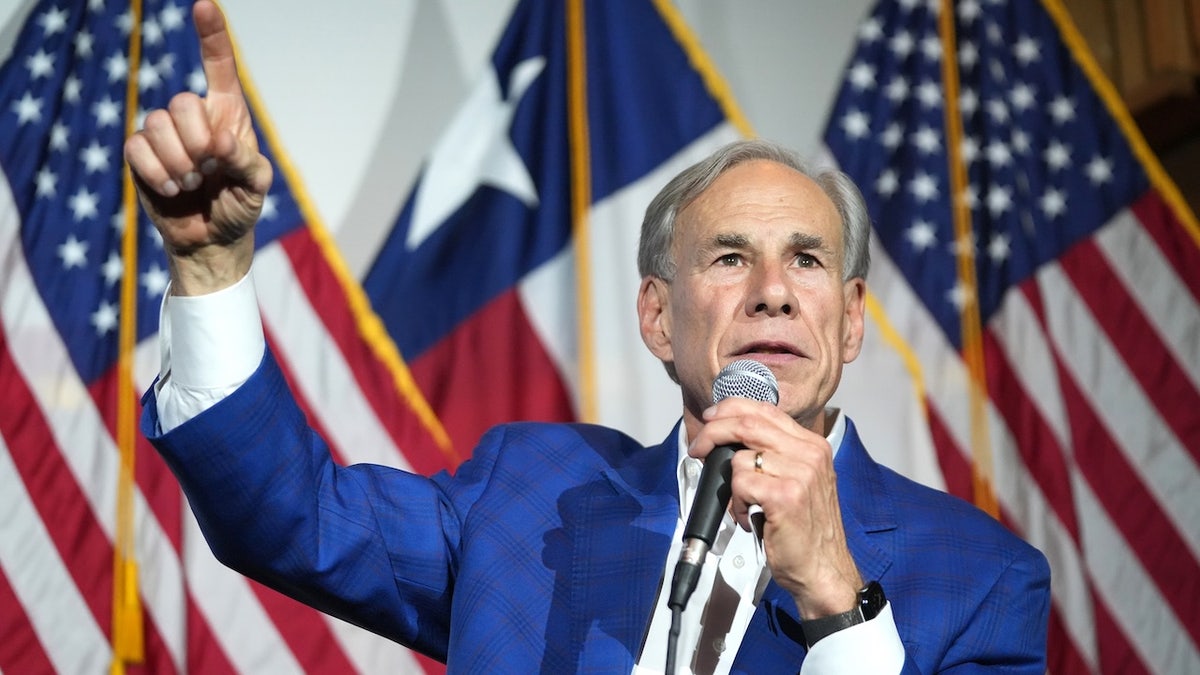 Texas GOP Gov. Greg Abbott points up in front of an American flag