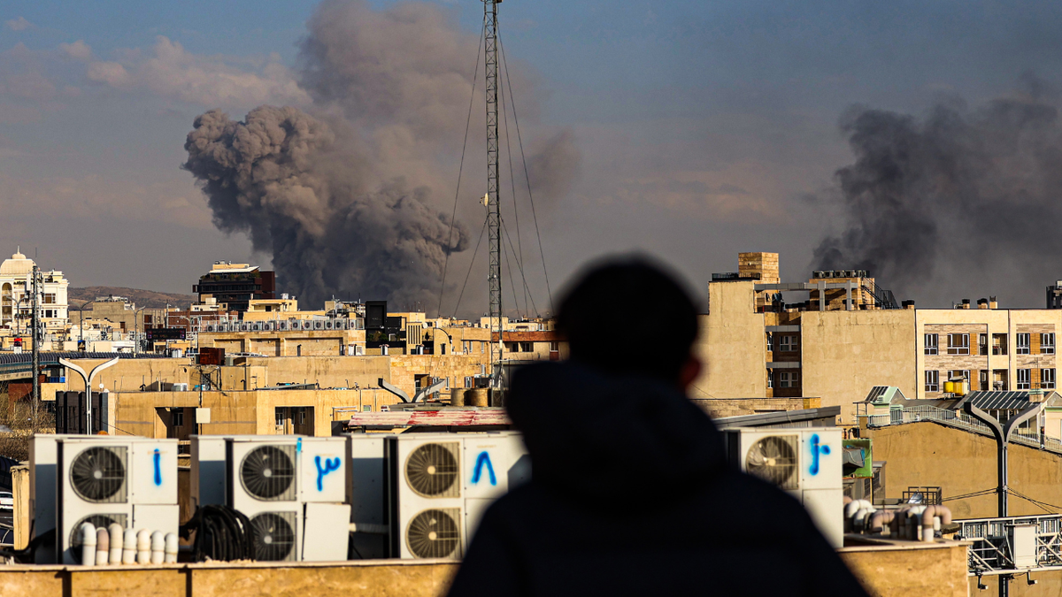 A person watches a smoke plume rise in the distant in Tehran, Iran on March 2, 2026.