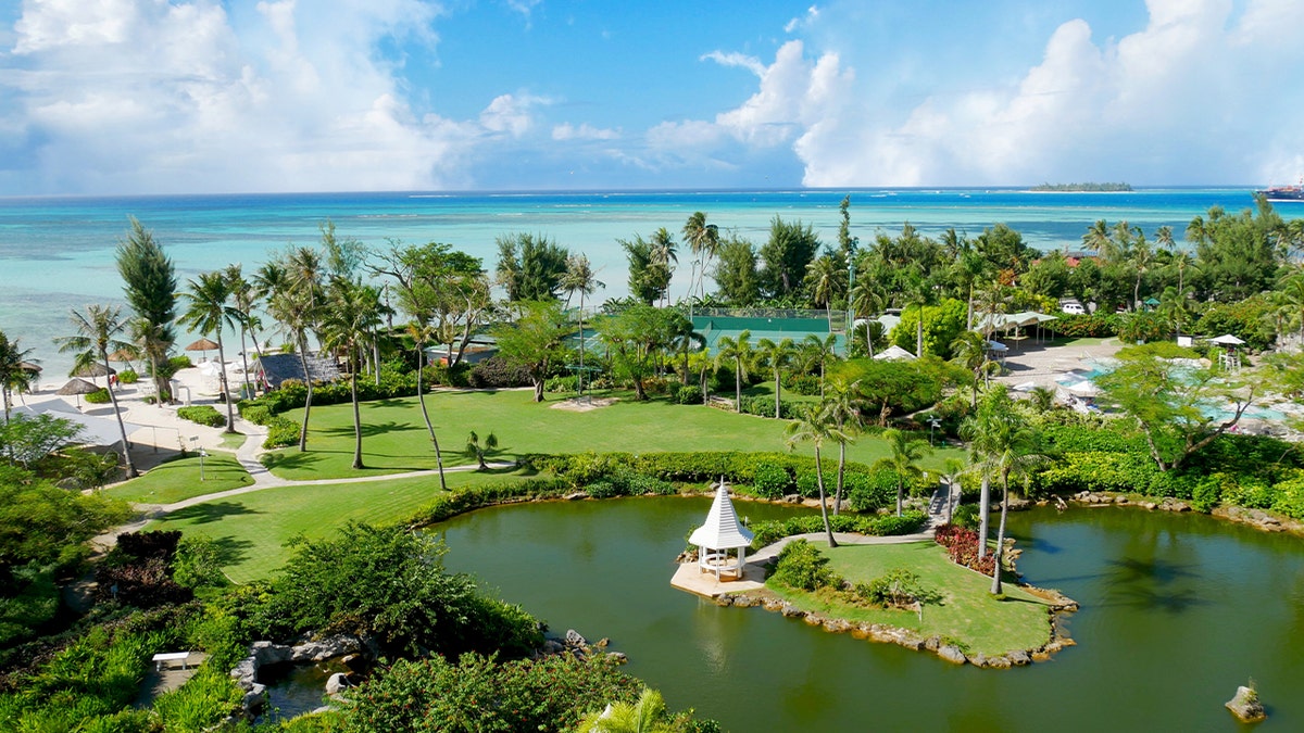 Pristine blue waters of the Micro Beach and the far-off Managaha Island backdrops a perfectly manicured garden with pond in Saipan, Northern Mariana Islands.