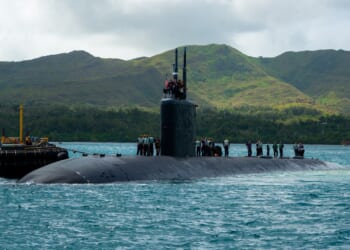 A Los Angeles-class attack submarine seen near a port, with hills in the background.