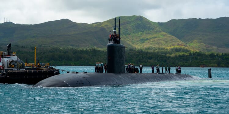 A Los Angeles-class attack submarine seen near a port, with hills in the background.