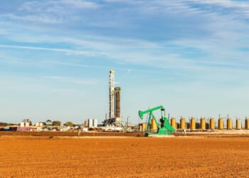 A drilling rig and pumpjack in the Permian Basin in the southwestern United States, surrounded by storage tanks.