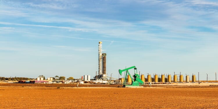 A drilling rig and pumpjack in the Permian Basin in the southwestern United States, surrounded by storage tanks.