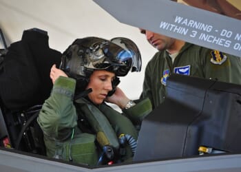 An F-35 pilot putting on her helmet inside the plane's cockpit.