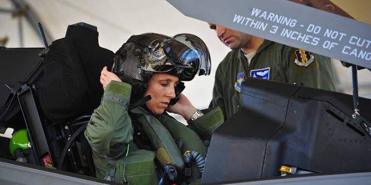 An F-35 pilot putting on her helmet inside the plane's cockpit.