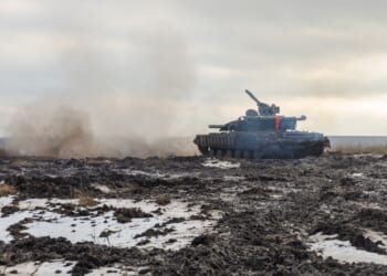 A Ukrainian tank firing its main gun on a muddy battlefield.