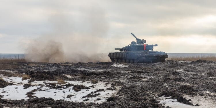 A Ukrainian tank firing its main gun on a muddy battlefield.