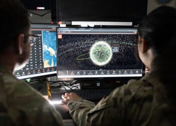 Two US Space Force soldiers looking at a computer screen with satellite positions on it.