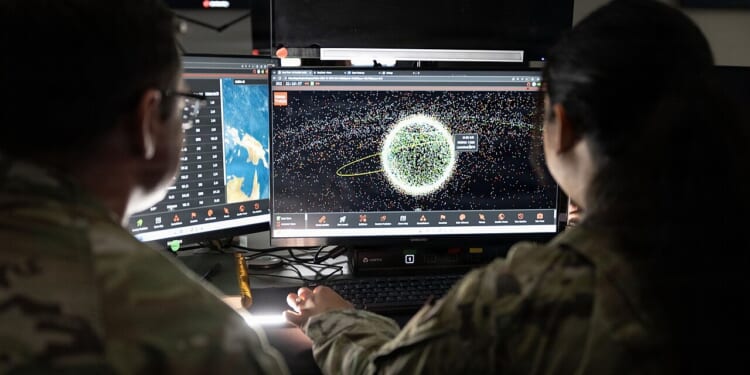 Two US Space Force soldiers looking at a computer screen with satellite positions on it.