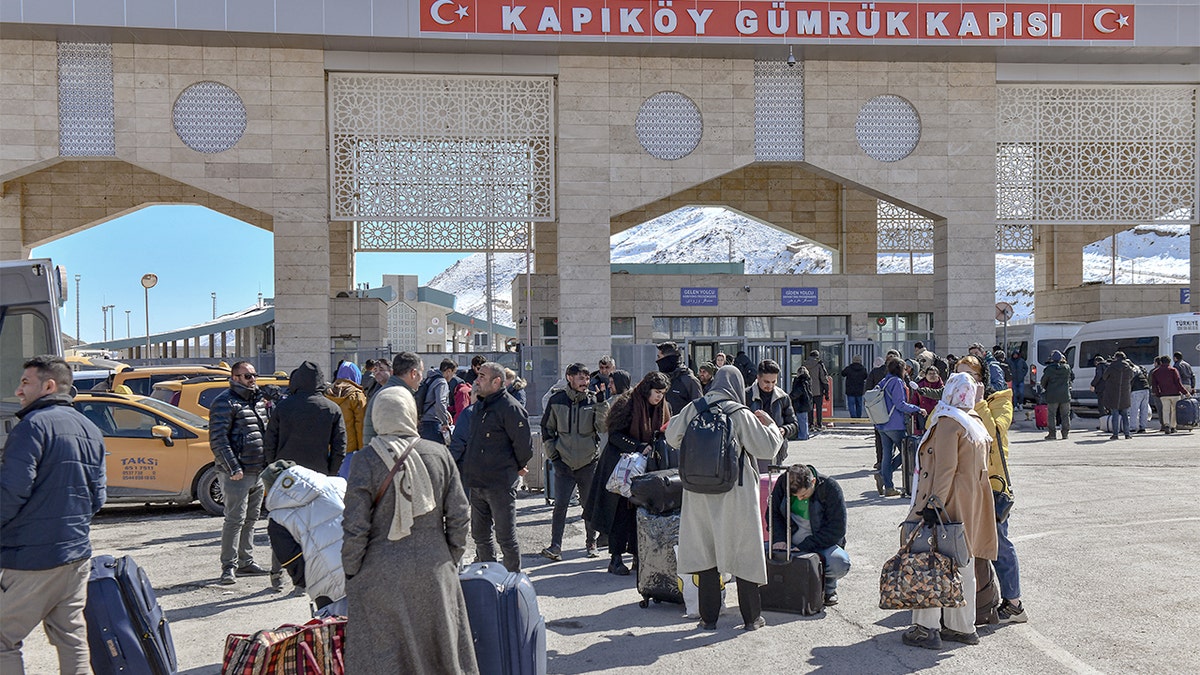 A group of Iranian nationals walk through a border gate into Turkey with luggage and belongings visible.