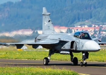 A JAS 39 Gripen fighter jet on an airfield runway.