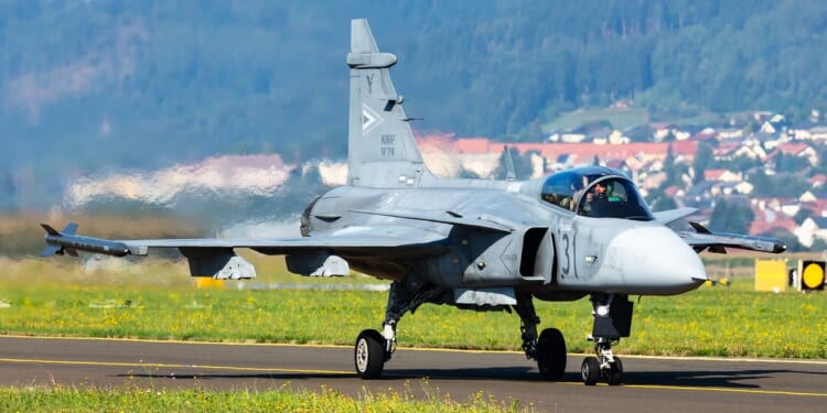 A JAS 39 Gripen fighter jet on an airfield runway.