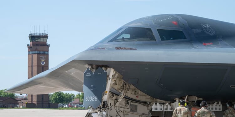 Several airmen stand underneath a B-2 Spirit's cockpit, illustrating its enormous size.