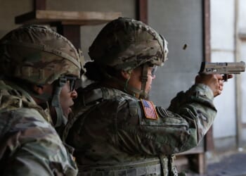 A soldier firing a Sig Sauer M17 pistol at a gun range.