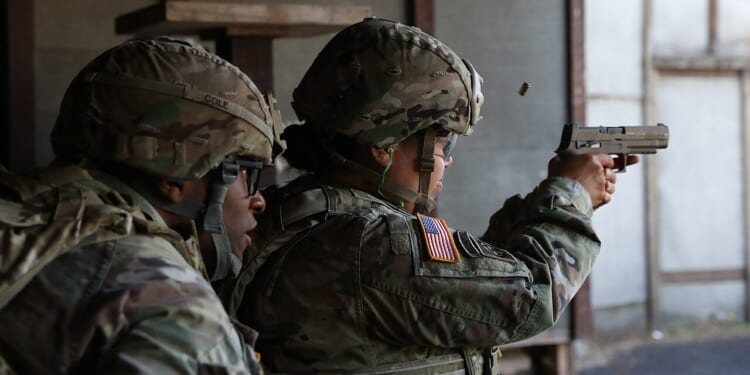 A soldier firing a Sig Sauer M17 pistol at a gun range.