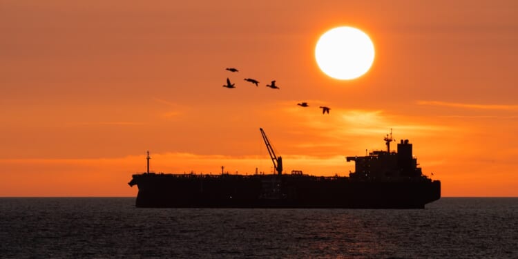 An oil tanker seen in shadow at dusk.